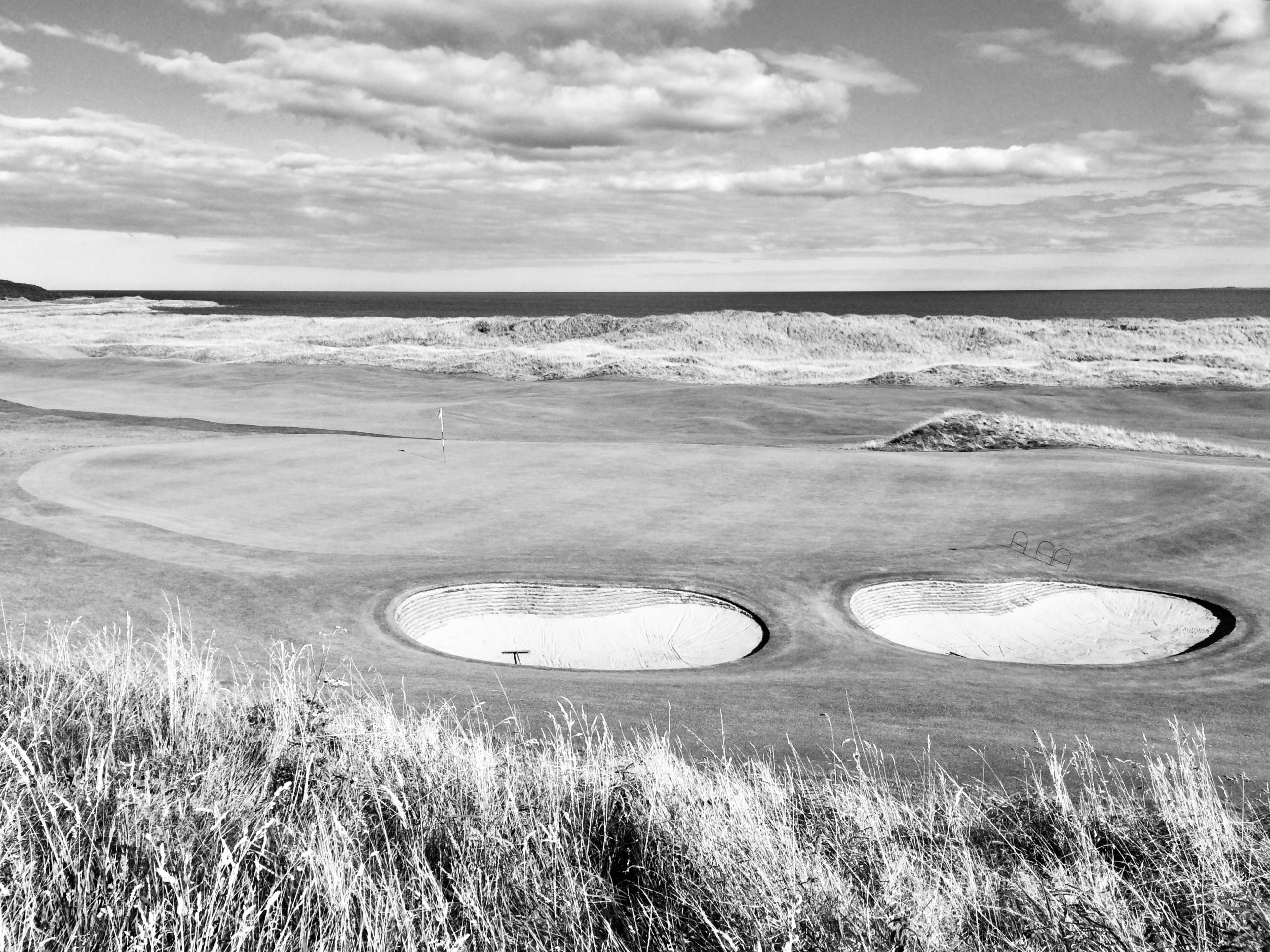Black and white photograph of Royal Dornoch’s 4th green with the North Sea in the background, showcasing classic Scottish links golf and dramatic coastal scenery.