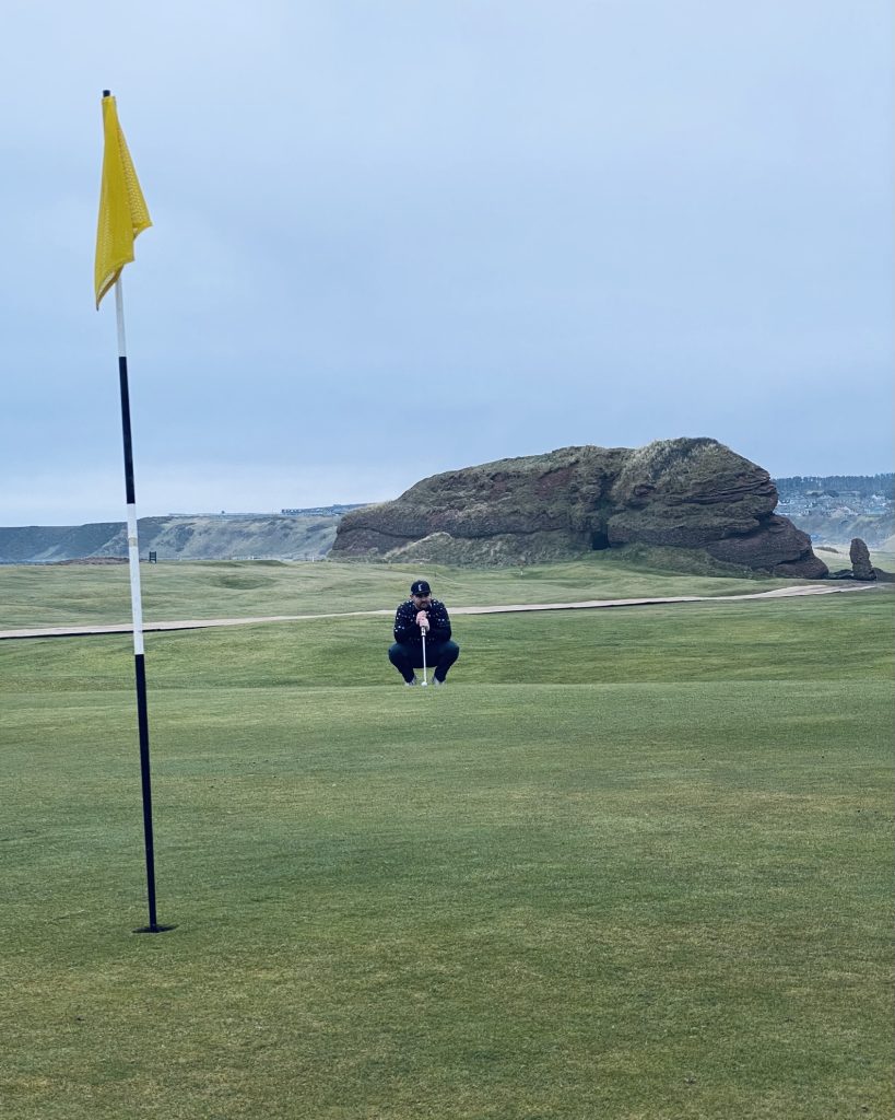Golfer lining up a putt on the green at Cullen Links, with the course’s iconic red sandstone rock formations rising in the background.