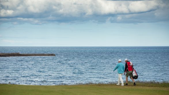 Golfer and caddie walking at Royal Dornoch with the Dornoch Firth behind