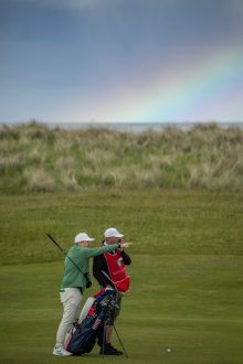 Golfer preparing for his second shot on the 14th hole with a rainbow behind