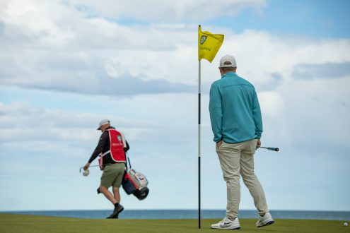 Golfer and caddie on a Royal Dornoch green with the Dornoch Firth behind